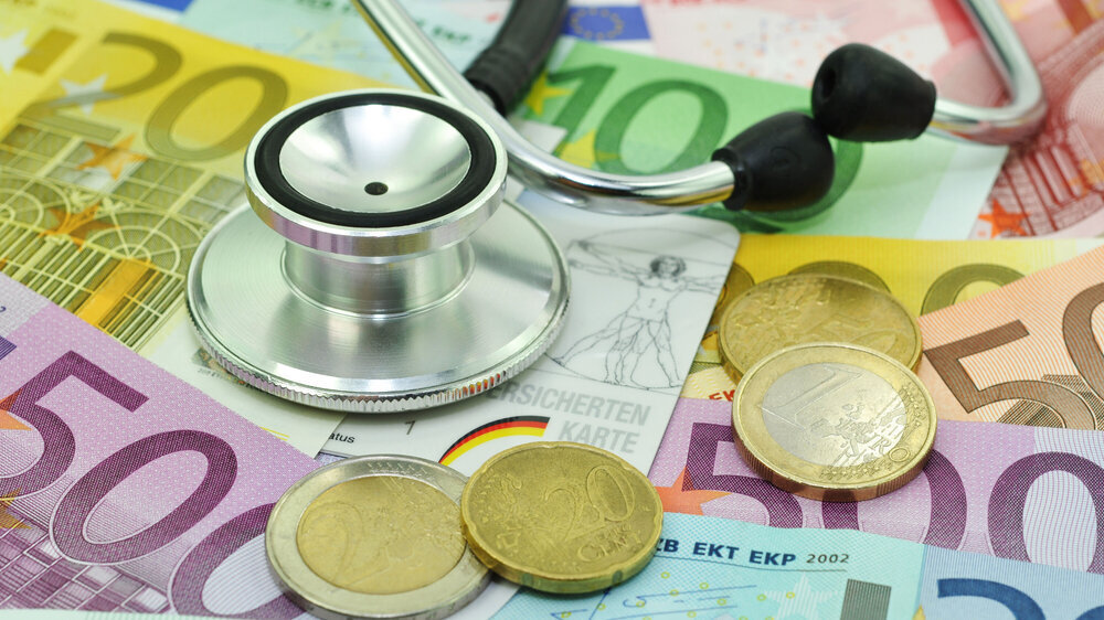 Geld, Schein und Münzen auf denen ein Stethoskop liegt. Geld, Schein und Münzen auf denen ein Stethoskop liegt.