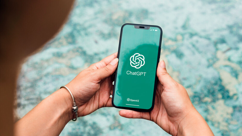 Mädchen im Park hält ein Smartphone mit der Chatbot-App ChatGPT.