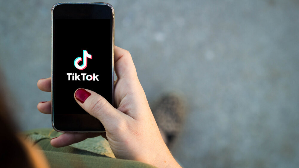 Eine Hand hält ein Smartphone, auf dessen Bildschirm das TikTok-Logo zu sehen ist