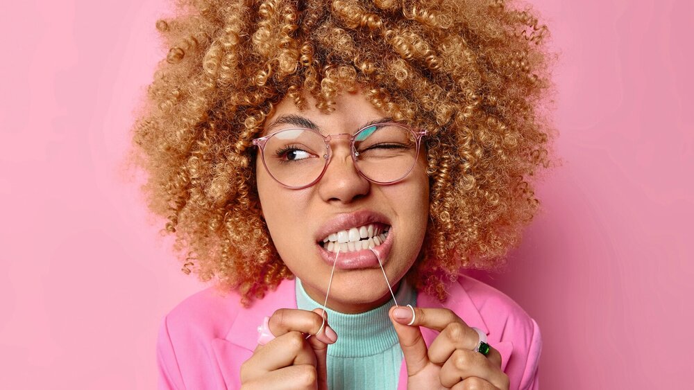 Junge Frau mit Brille und Afrolook nutzt Zahnseide