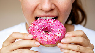 Close-up of a woman eating a donut with pink glaze.
