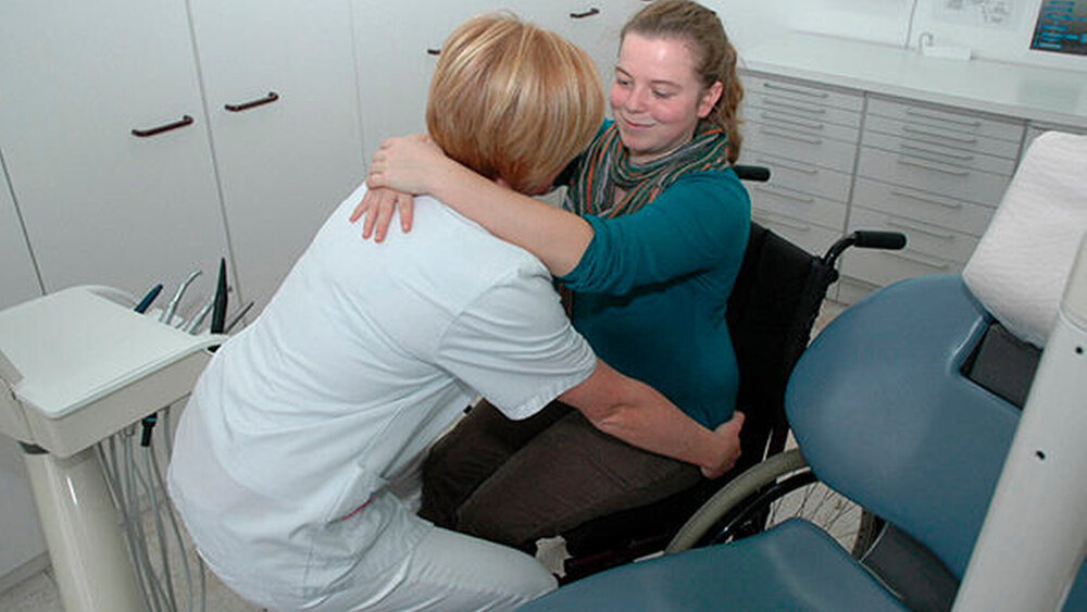 Abb. 5: Vor dem Aufstehen verlagert die betreuende Person ihr Schwergewicht etwas nach hinten. Entsprechend beugt sich die Patientin nach vorne. Auf diese Weise ist es möglich, ohne viel Kraftaufwand langsam und sicher aufzustehen. |