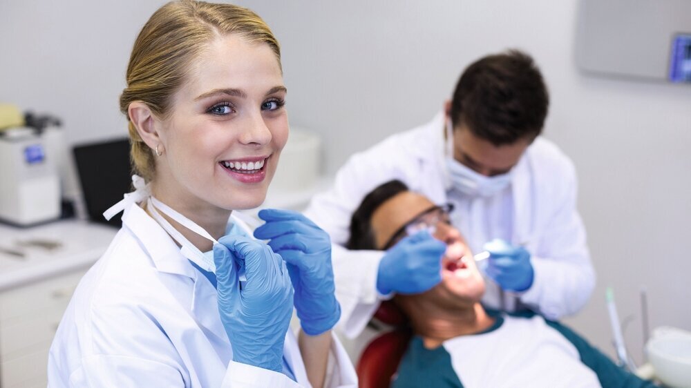 Portrait of smiling dentist standing while her colleague examining patient in background ZFA