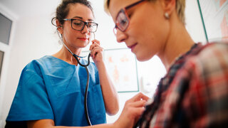 Krankenhausärztin untersucht Patientin mit Stethoskop.