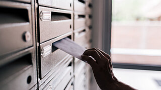 Hand steckt Brief in Briefkasten