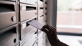 Hand steckt Brief in Briefkasten