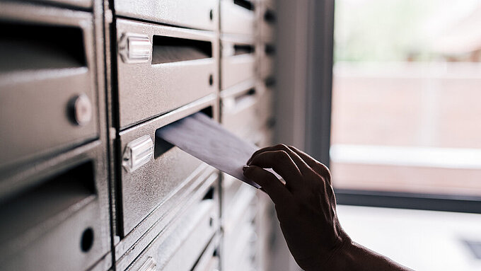 Hand steckt Brief in Briefkasten