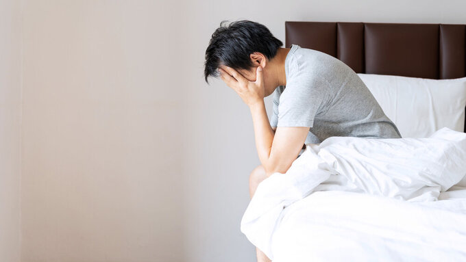 Gestresster oder depressiver Mann stützt auf dem Bett sitzend den Kopf in die Hände