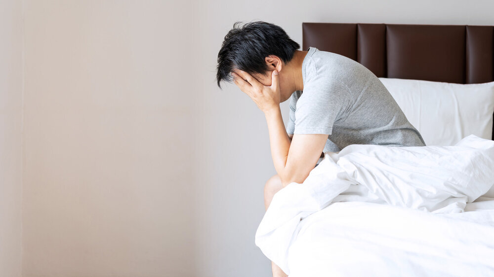 Gestresster oder depressiver Mann stützt auf dem Bett sitzend den Kopf in die Hände