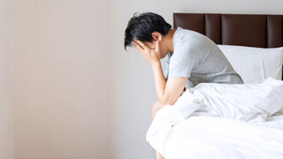 Gestresster oder depressiver Mann stützt auf dem Bett sitzend den Kopf in die Hände