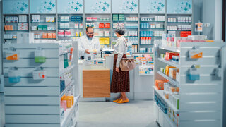 Kundin steht vor dem Schalter der Apotheke und bezahlt. Apotheker bedient Kundin.