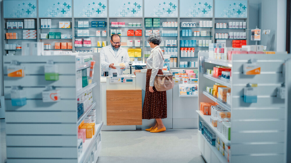 Kundin steht vor dem Schalter der Apotheke und bezahlt. Apotheker bedient Kundin. Kundin steht vor dem Schalter der Apotheke und bezahlt. Apotheker bedient Kundin.
