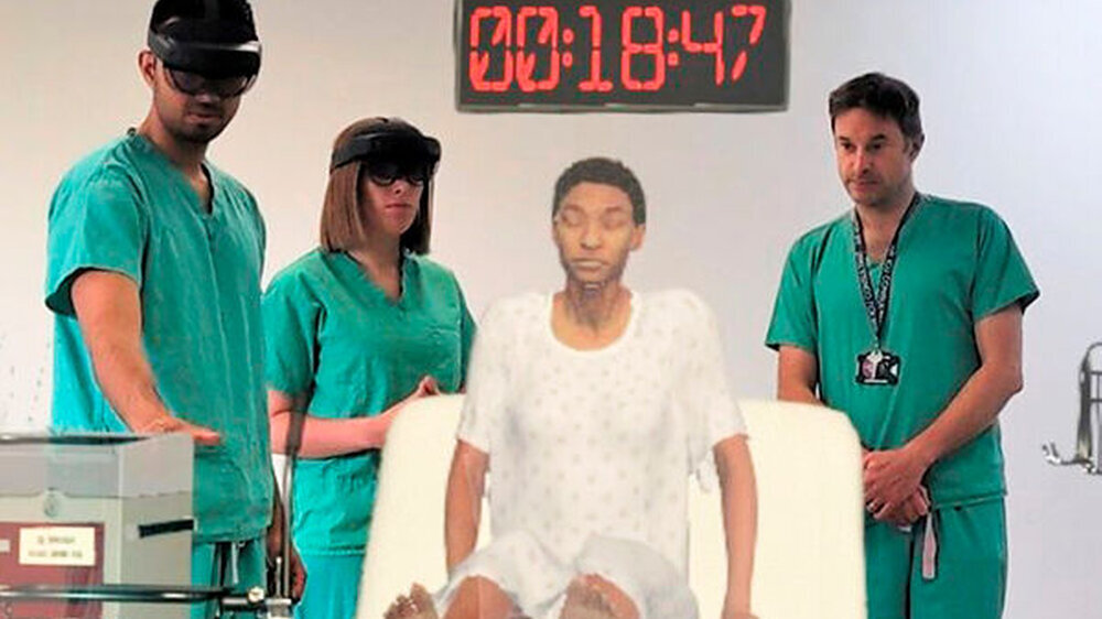 Bei der Übung tragen die angehenden Mediziner Headsets mit einer integrierten Virtual Reality-Brille, können sich aber weiterhin gegenseitig sehen und schauen gemeinsam auf die Simulation, also die Hologramm-Patientin. Diese zwei Ebenen der Sinneswahrne
