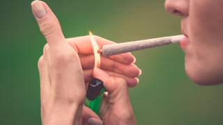Nahaufnahme einer Frau, die einen Marihuana-Joint mit einem Feuerzeug und einer großen Flamme anzündet.
