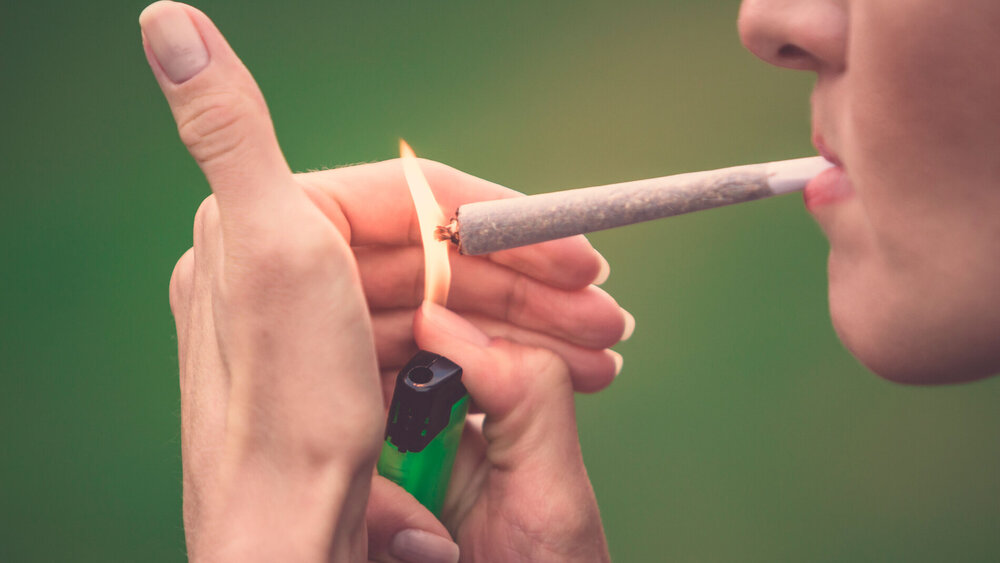 Nahaufnahme einer Frau, die einen Marihuana-Joint mit einem Feuerzeug und einer großen Flamme anzündet.