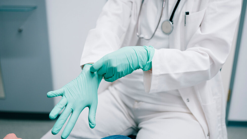 Junge Ärztin zieht sich vor der Behandlung Handschuhe an