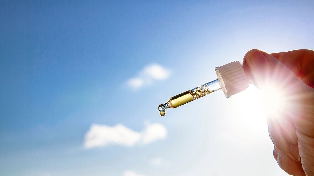 Hand holding dropper pipette with nice golden liquid D-vitamin against sun and blue sky on sunny day. Vitamin D keeps you healthy while lack of sun in winter, cure concept.