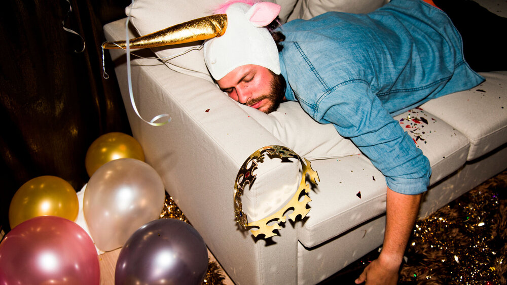 Ein Mann hängt nach einer Party schlafend auf der Couch.