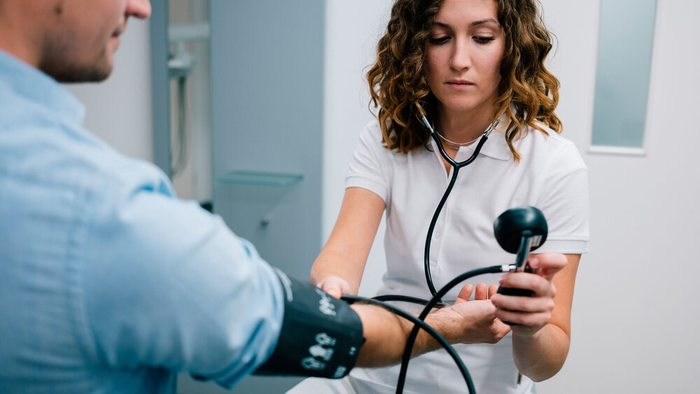 Junge Ärztin misst den Blutdruck eines Patienten.