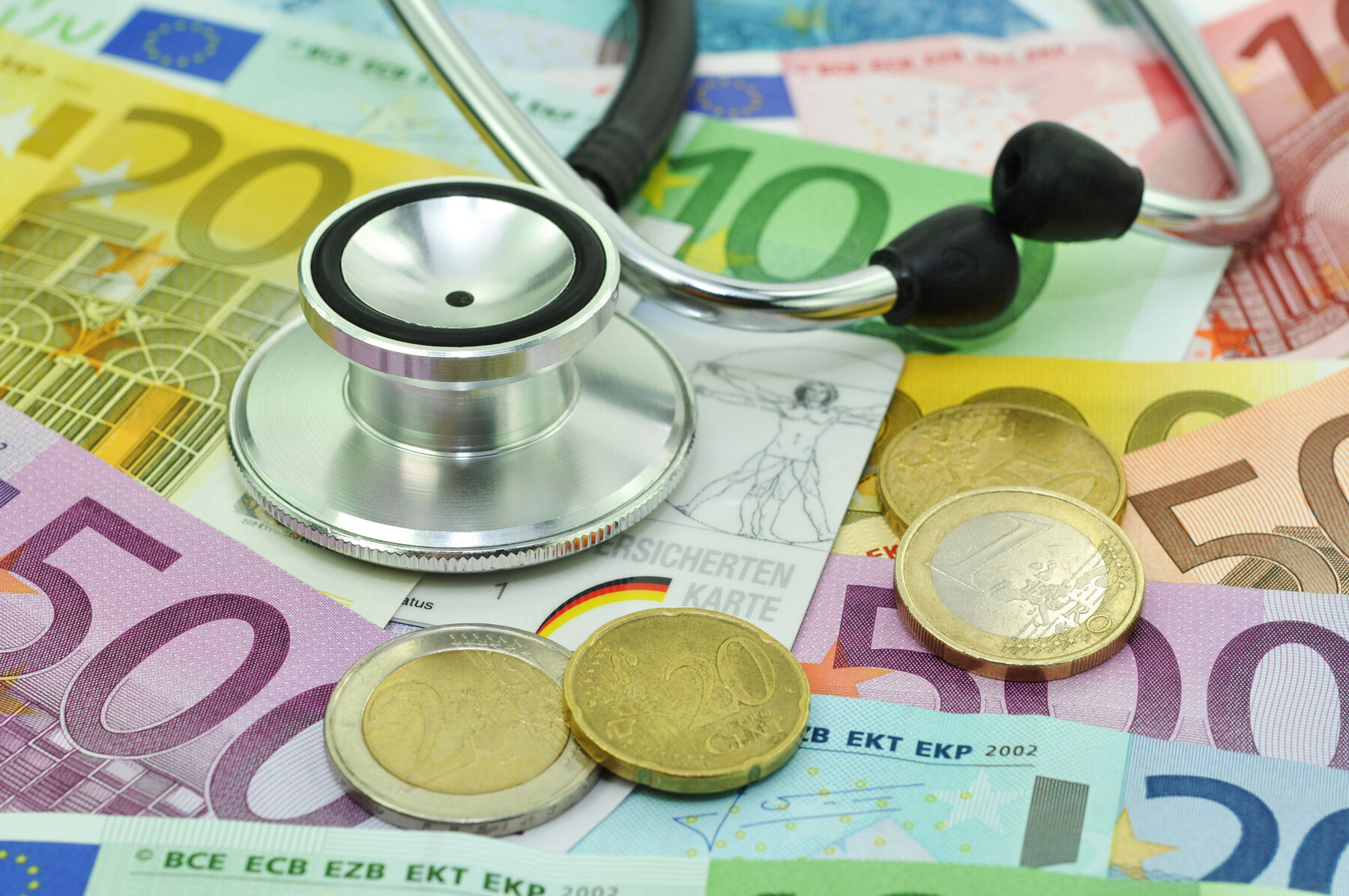 Geld, Schein und Münzen auf denen ein Stethoskop liegt. Geld, Schein und Münzen auf denen ein Stethoskop liegt.
