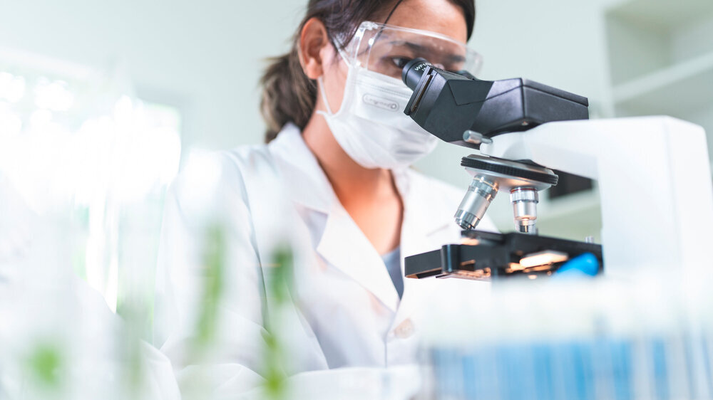 Laborantin mit Augen- und Mundschutz arbeitet am Mikroskop. Laborantin mit Augen- und Mundschutz arbeitet am Mikroskop.