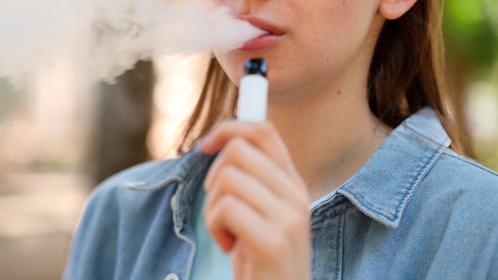 Young woman using electronic smoking device outdoors, closeup