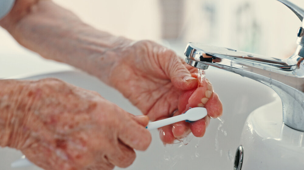 Dentures, senior person and brushing teeth for hygiene with dental care, bacteria removal and fresh breath. Oral wellness, hands and toothbrush for health, plaque prevention and healthy mouth in home.