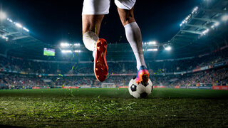 Soccer player stepping on ball during night match in stadium. Concept of ball control, tactical pause, sport footwear advertising, match promo, and team strategy visuals.