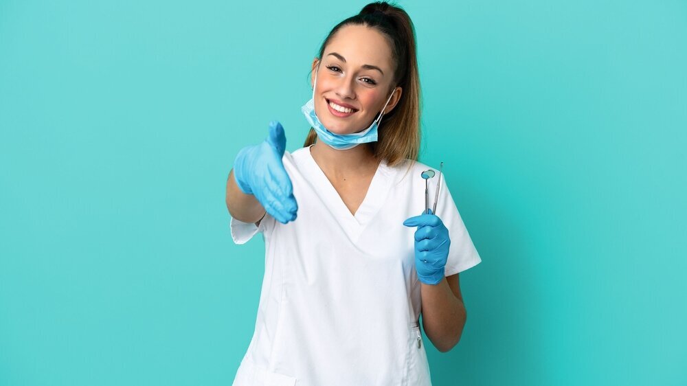 Dentist caucasian woman holding tools isolated on blue background shaking hands for closing a good deal Dentist caucasian woman holding tools isolated on blue background shaking hands for closing a good deal
