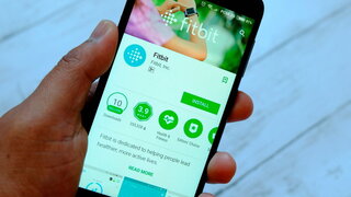Eine männliche Hand hält ein Smartphone mit Fitbit-Apps auf einem androiden Google Play Store