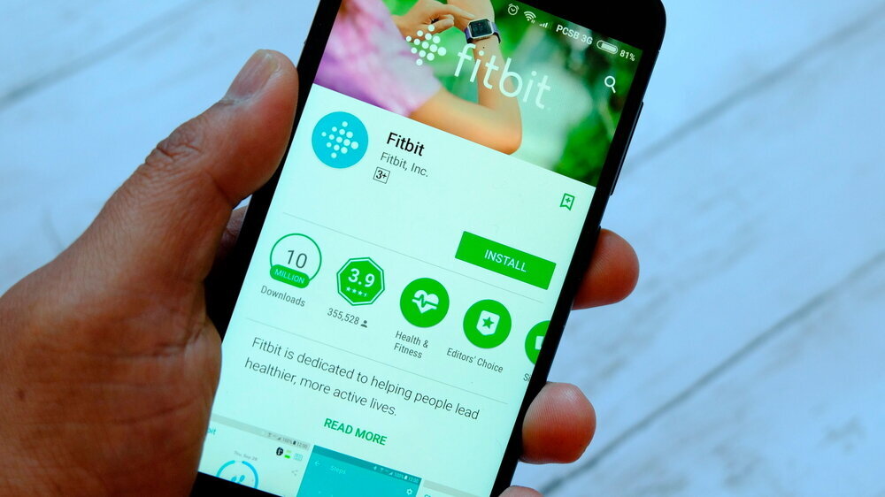 Eine männliche Hand hält ein Smartphone mit Fitbit-Apps auf einem androiden Google Play Store