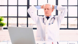 Shot of careworn male doctor sitting behind his laptop in doctor’s office.