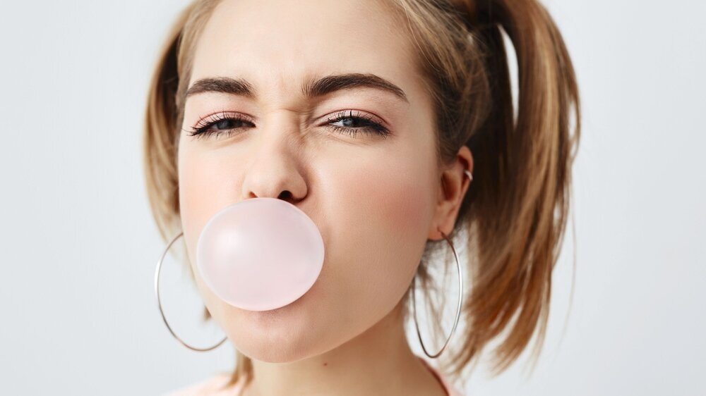 Stilvolles, charmantes, hübsches Mädchen im Teenageralter mit zwei Pferdeschwänzen, das die Augen verdreht und ein rosa Kaugummi im Mund hat