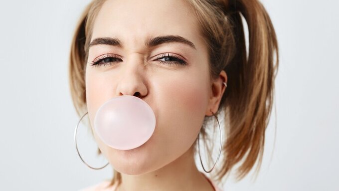 Stilvolles, charmantes, hübsches Mädchen im Teenageralter mit zwei Pferdeschwänzen, das die Augen verdreht und ein rosa Kaugummi im Mund hat