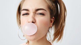 Stilvolles, charmantes, hübsches Mädchen im Teenageralter mit zwei Pferdeschwänzen, das die Augen verdreht und ein rosa Kaugummi im Mund hat