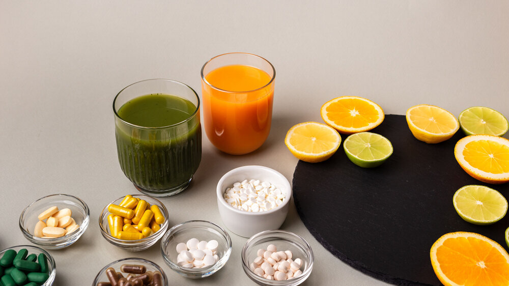 Nutritional supplements, various vitamins and minerals, pills from above on a black stone desk on green background. Smoothie, citrus fruits - lemon, orange and lime as a source of natural vitamins.
