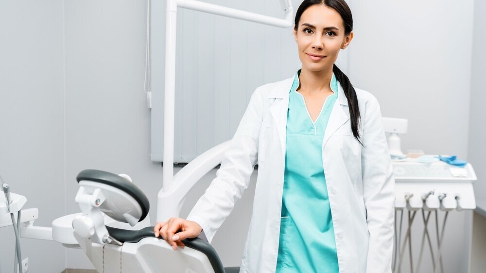 attractive dentist standing near chair in dental clinic attractive dentist standing near chair in dental clinic