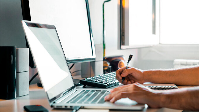 Person working from home at their desk with computers Person working from home at their desk with computers