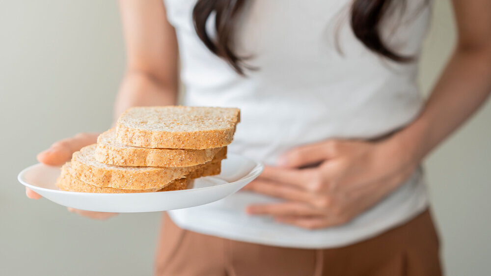 Gluten allergy, asian young woman hand holding, refusing to eat white bread slice on plate in breakfast food meal at home, girl having a stomach ache. Gluten intolerant and Gluten free diet concept. Glutenallergie