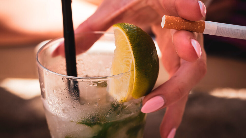 Die Hand einer Frau hält einen Longdrink und eine Zigarette.