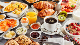 Huge healthy breakfast spread on a table with coffee, orange juice, fruit, muesli, smoked salmon, egg, croissants, meat and cheese