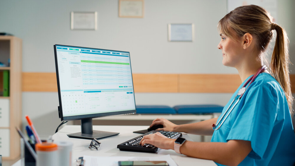 Hispanic Doctor's Office: Experienced Head Nurse Sitting at Her Desk Working on Personal Computer in Data Software. Medical Health Care Specialist Filling Prescription Forms, Checking Analysis Results MFA, Praxisempfang