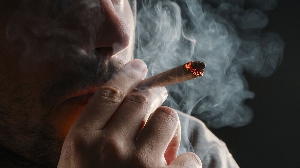 Man smoking a marijuana weed joint, inhaling cannabis smoke. Den ganzen Tag Joints rauchen und damit Geld verdienen - ein Traumjob?