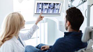 Zahnärztin zeigt im Gespräch mit einem Patienten auf einen Monitor