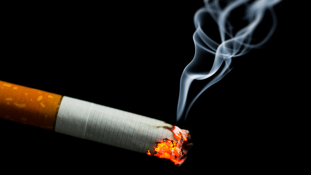 Brennende Zigarette vor schwarzem Hintergrund.