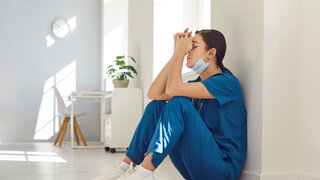 Müde, deprimierte Krankenschwester mit blauer Gesichtsmaske und Uniform sitzt auf dem Krankenhausboden.