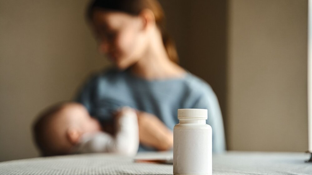 Mother breastfeeding her cute newborn Blurred view of the calm caucasian mother breastfeeding her cute newborn son and looking to him with smile while sitting with baby at the light sunny kitchen. Focus at the table with pills