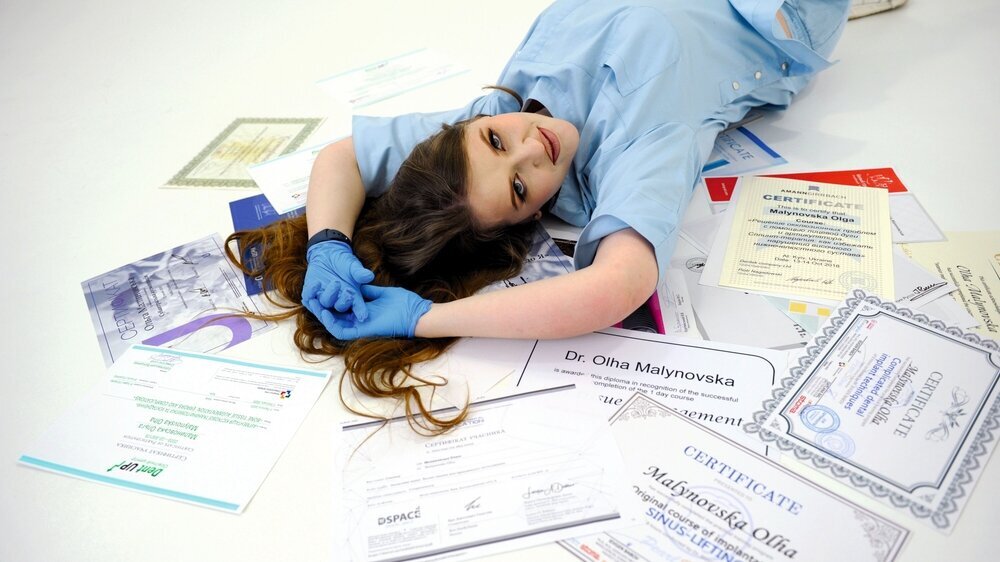 beautiful woman doctor in gloves and blue medical suit lies on her diplomas certificates on the white floor medical education training courses doctor nurse dentist stomatology high qualification Zahnmedizinstudentin Bachelor Prüfung Approbation
