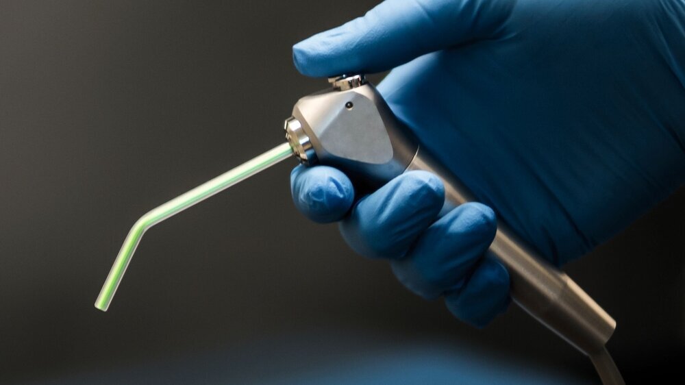 Hand in blue latex glove holding a dental air water syringe.