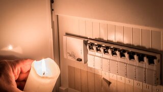Sicherungskasten mit Sicherungen in einem Verteilerkasten während eines Stromausfall mit weißer Kerze beleuchtet die ein Mann in der Hand hält, Deutschland